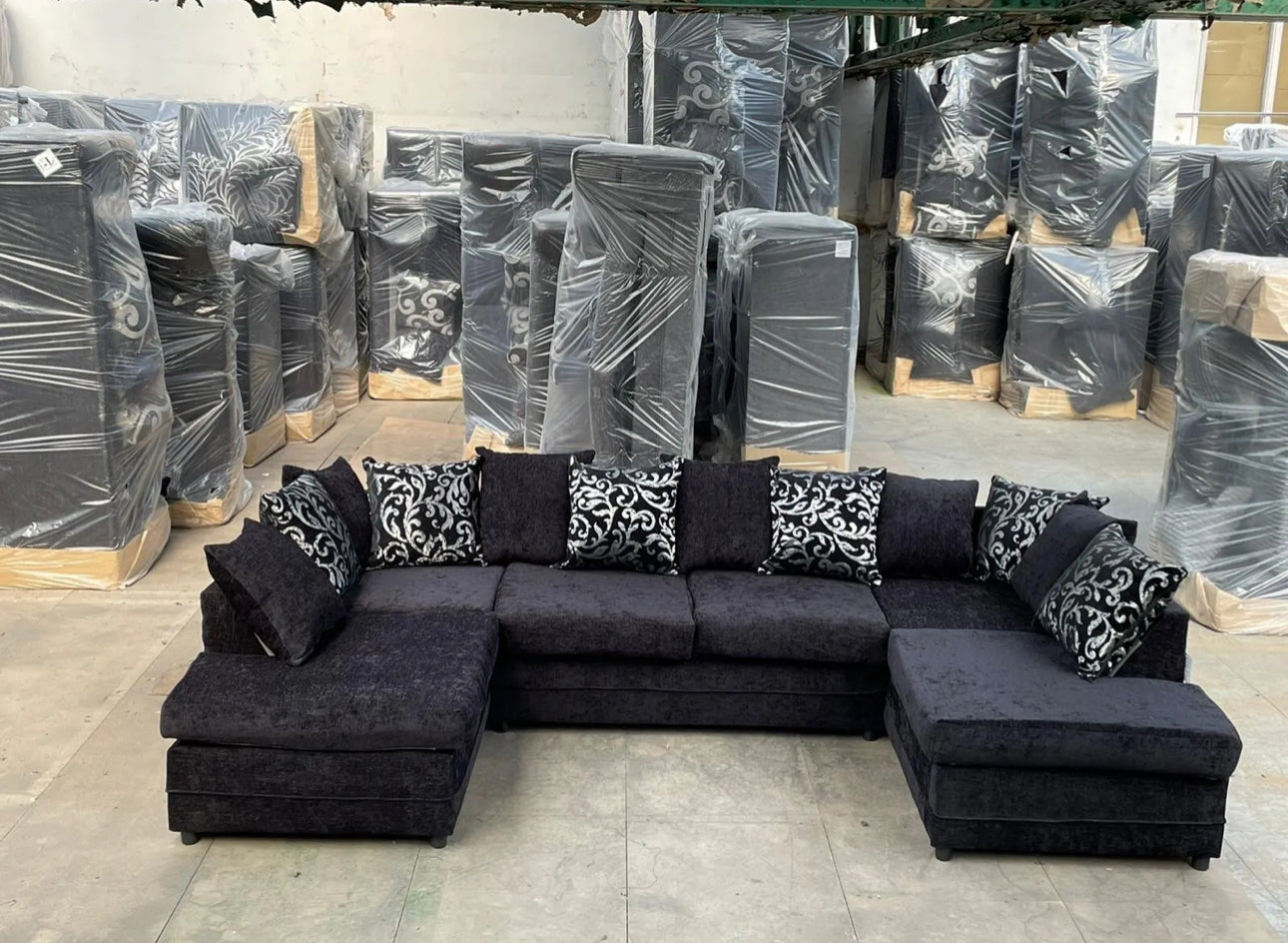 Furnish UK U shape fabric sofa with cushions in dark upholstery and patterned pillows in a warehouse setting
