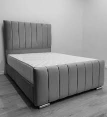 Modern black panel headboard bed with padded frame and mattress on wooden floor by Furnish UK