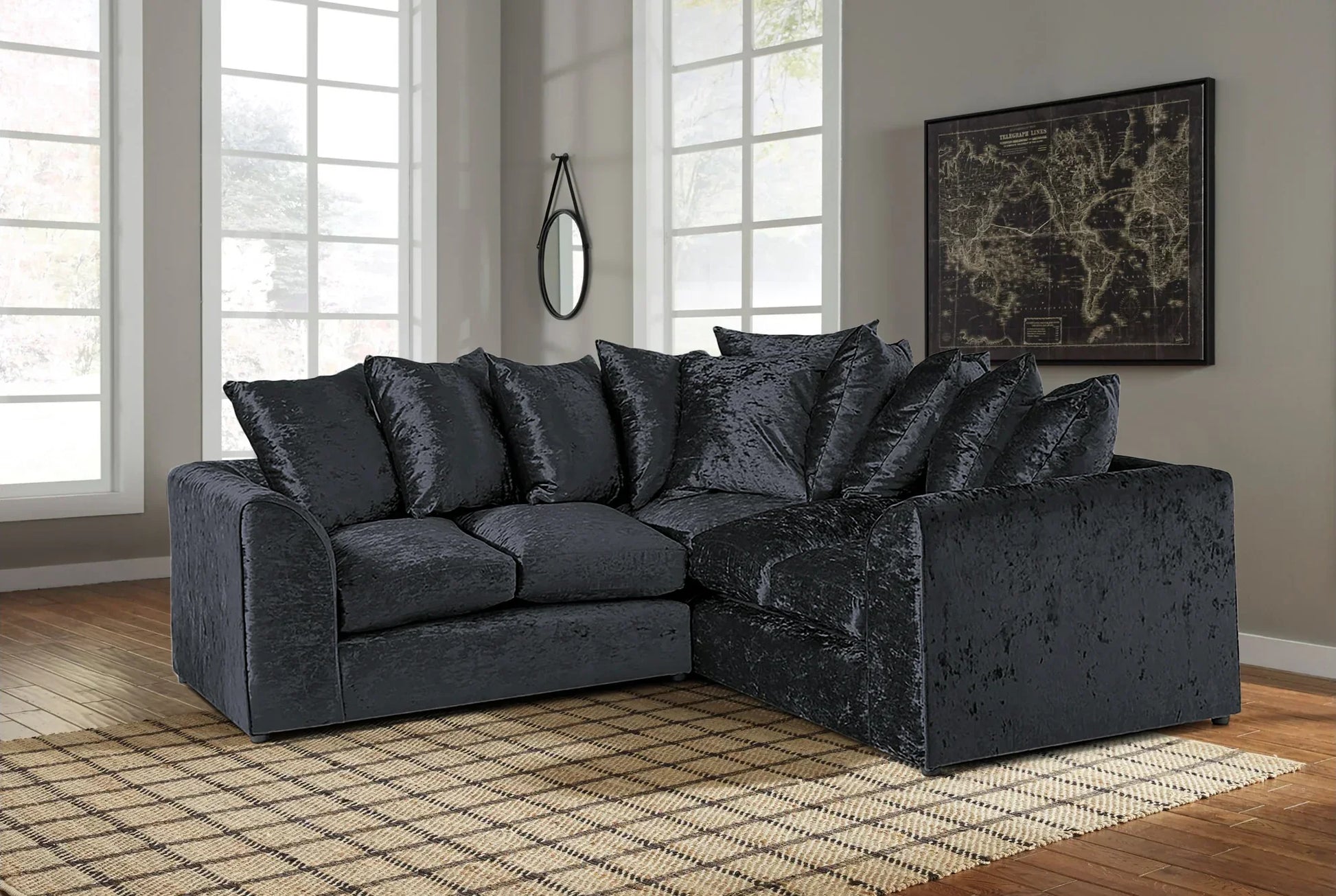 Black crush velvet corner sofa with multiple cushions in a bright living room setting by Furnish UK