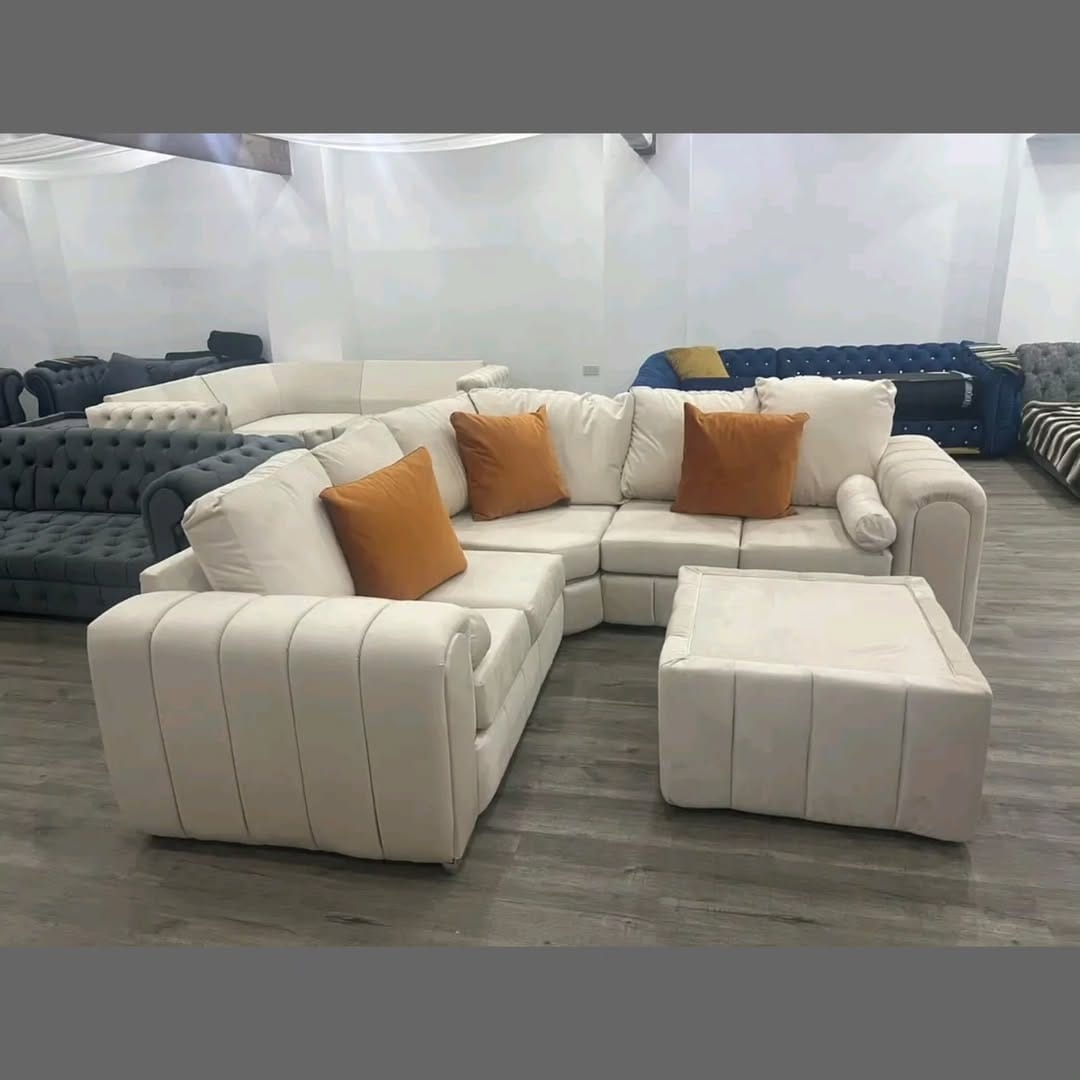 Furnish UK modern L-shaped sofa in white with orange throw pillows and matching ottoman on wooden floor