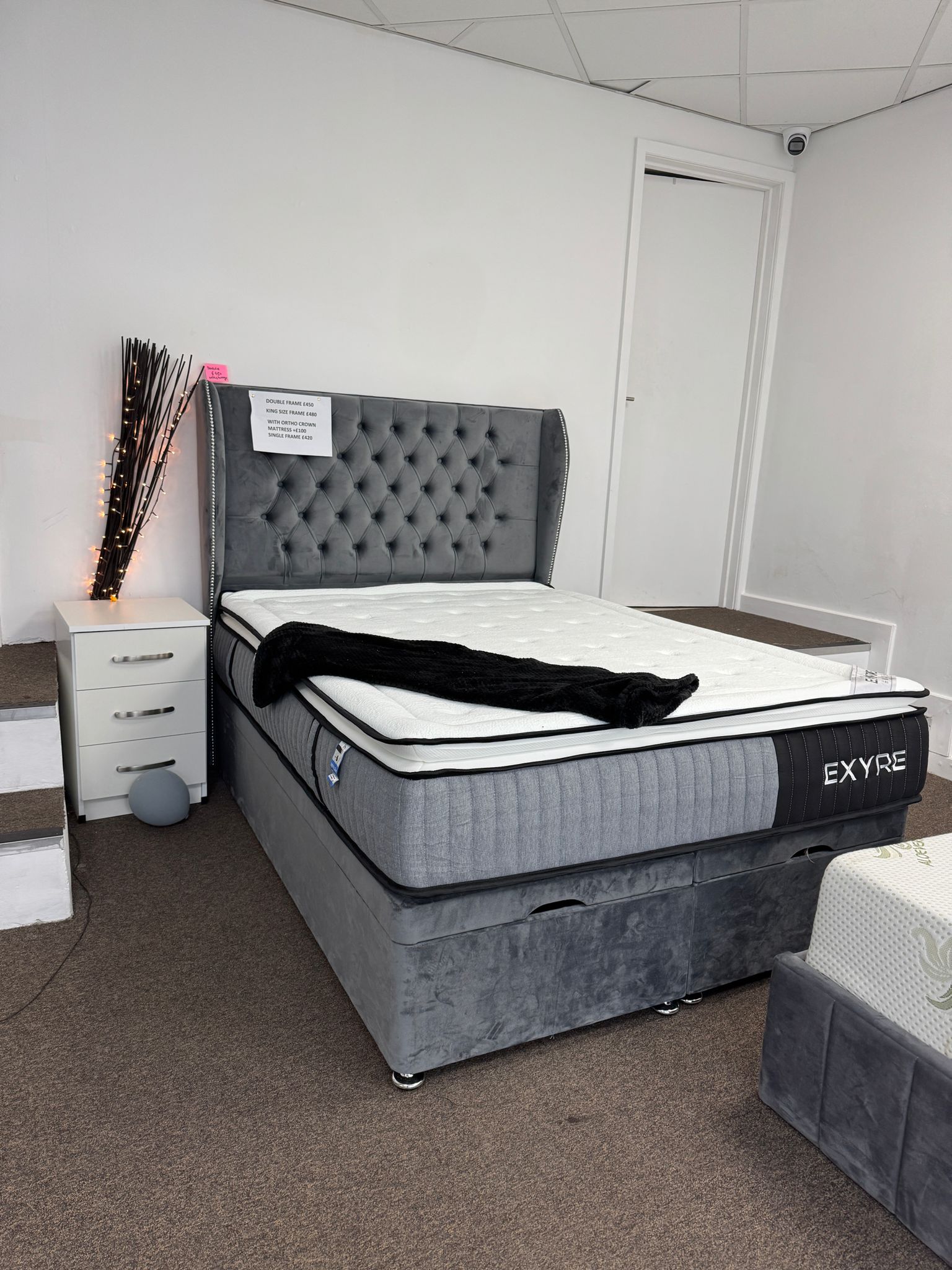 Furnish UK grey ottoman divan bed with storage and tufted headboard in showroom setting